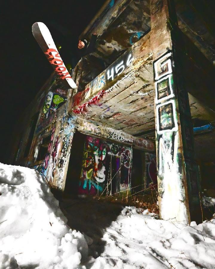 Snowboard leaning against a graffiti-covered wall with snow on the ground